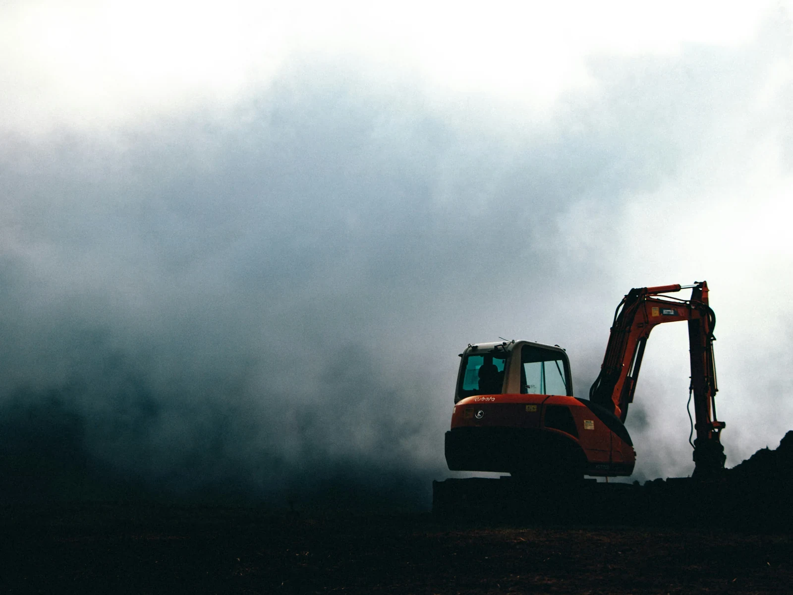 A mini excavator silhouetted against a cloud of dust on site